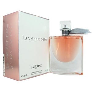 May include: A perfume bottle and box set. The box is white and rose-gold with the text "La vie est belle". The perfume bottle is clear with a peach-colored liquid inside. The bottle has a silver cap and a gray ribbon.