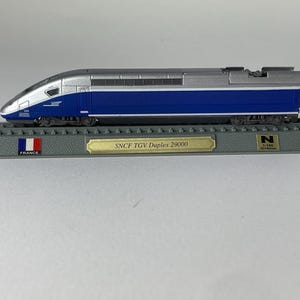 Könnte beinhalten: Ein Modell des SNCF TGV Duplex 29000 Zuges in Blau und Silber, montiert auf einem grauen Schienen-Display-Sockel. Der Sockel zeigt eine französische Flagge, ein goldenes Schild mit der Aufschrift SNCF TGV Duplex 29000 und ein N 1:160 Etikett.