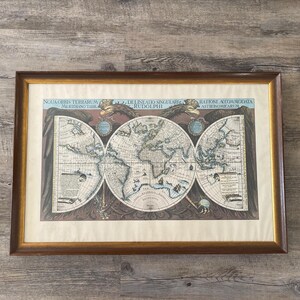 Könnte beinhalten: Gerahmter Vintage-Weltkarten-Druck mit einem goldfarbenen Holzrahmen. Die Karte zeigt detaillierte Illustrationen von Kontinenten und Ozeanen mit lateinischem Text. Das Kunstwerk wird auf einem hellen Hintergrund angezeigt.