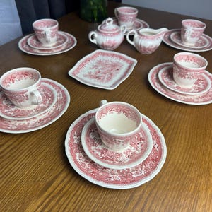 May include: A tea set featuring cream-colored ceramic pieces with a red floral transferware pattern. The set includes five teacups, five saucers, five small plates, a lidded sugar bowl, a creamer, and a small rectangular serving tray.