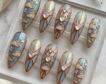 May include: Set of ten long, almond-shaped false nails. Each nail features a stained-glass design with a blue sky, clouds, and a heart or star. The nails have a copper-colored outline and iridescent accents.