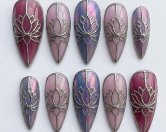 May include: A set of ten almond-shaped press-on nails featuring a stained-glass effect. Each nail has a silver-toned metal outline of a lotus flower over a base of varying shades of pink, magenta, and iridescent blue-purple shimmer.