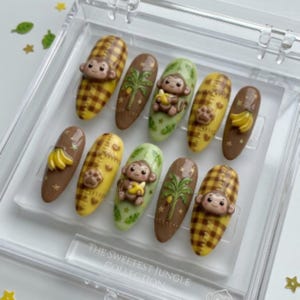 Könnte beinhalten: Ein Set aus zehn künstlichen Nägeln mit Dschungel-Thema. Die Nägel zeigen verschiedene Designs, darunter Affen, Bananen, Palmen und Karomuster. Die Farbpalette umfasst Braun, Gelb und Grün, mit dem Text "THE SWEETEST JUNGLE COLLECTION".