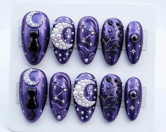 May include: A set of ten purple press-on nails with celestial designs. Each nail features a glossy finish and is adorned with black cats, crescent moons, constellations, and pearl accents. The nails are arranged on a white display card.