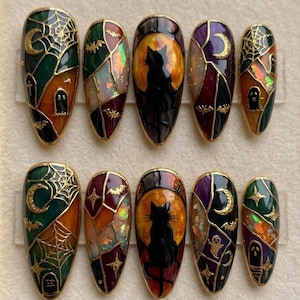 May include: Set of ten Halloween-themed press-on nails. Each nail features a unique design with a gold outline, including a black cat silhouette against an orange moon, spiderwebs, bats, and ghosts. The nails have a glossy finish.