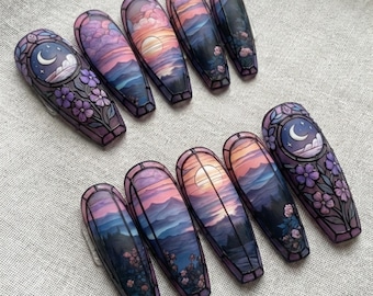May include: Set of ten coffin-shaped false nails with a stained-glass design. Each nail features a landscape scene with a sunset, mountains, and floral accents. The color palette includes purple, blue, and orange hues.