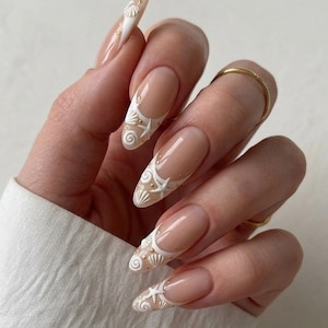 May include: Long, almond-shaped nails with a French manicure design. The nails feature a clear base with white tips adorned with seashell and starfish designs. Gold accents are scattered throughout the design.