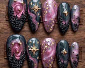 May include: Set of ten oval-shaped false nails with a celestial theme. Each nail features a dark teal base with pink and purple swirls, gold stars, and forest silhouettes. Some nails have gold starburst accents.