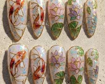 May include: A set of ten artificial nails with a pearlescent base and gold trim. Designs include koi fish, lotus flowers, and lily pads in shades of orange, pink, purple, green, and blue. The nails are almond-shaped.