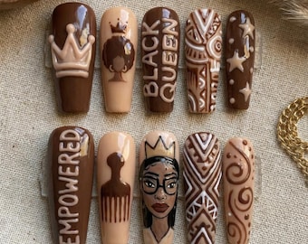 Könnte beinhalten: Ein Satz von zehn langen, Sarg-förmigen Kunstnägeln. Die Nägel weisen verschiedene Designs auf, darunter Kronen, die Wörter "BLACK QUEEN" und "EMPOWERED" sowie geometrische Muster. Die Farbpalette umfasst Brauntöne, Beige und Weiß.