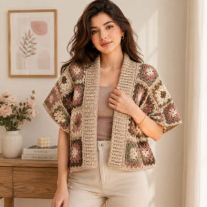 Op de afbeelding: Een gehaakt vest met een granny square patroon in tinten beige, oudroze en saliegroen. Het kledingstuk heeft een open voorzijde, korte mouwen en een geribbelde rand langs de kraag, gedragen over een effen beige top en een broek.