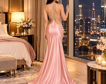 May include: A floor-length, light pink satin gown featuring a backless design with thin straps and a decorative lattice pattern of small white beads across the upper back. The dress has a fitted bodice that flows into a long, flared skirt.
