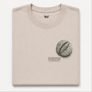 May include: A beige t-shirt with a crew neck. The shirt displays a graphic of a loaf of bread and the text "SOURDOUGH ENTHUSIAST - NATURALLY LEAVENED". The Moose Threads logo is at the top.