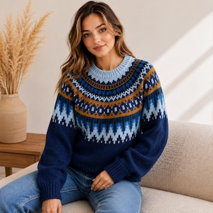 Op de afbeelding: Een gebreide trui met lange mouwen, een ronde hals en een veelkleurig fair isle-patroon over de borst en schouders. Het ontwerp bevat geometrische vormen in de kleuren marineblauw, lichtblauw en mosterdgeel.