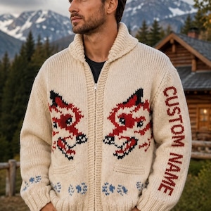 May include: A cream-coloured knit zip-up cardigan featuring a shawl collar and two front pockets. The garment displays a red and black fox pattern on the chest, blue floral accents along the hem, and the text CUSTOM NAME printed on the sleeve.