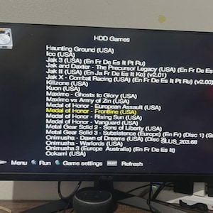 May include: A computer monitor displaying a black screen with a white text list titled HDD Games. The list includes titles such as Haunting Ground, Ico, Jak 3, Killzone, Maximo, Medal of Honor, Metal Gear Solid, Onimusha, and Okami with region tags.