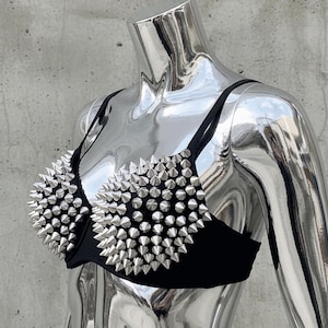 May include: Black bra with silver cone studs. The bra has thin black straps and is displayed on a chrome mannequin. The studs are densely packed, covering the cups of the bra.