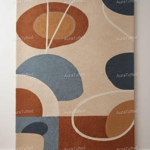 May include: A rectangular rug with an abstract design. The rug features geometric shapes in shades of brown, blue, and beige, with white accent lines. The rug is hanging on a white wall.