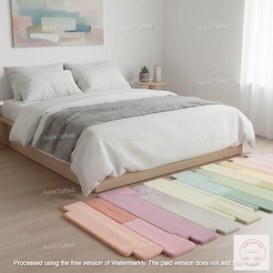 Könnte beinhalten: Ein Schlafzimmer mit einem Bett mit weißer Bettwäsche und einem grauen Überwurf. Bunte, pastellfarbene Teppiche im Dielen-Design liegen auf dem Boden. Ein Gemälde hängt über dem Bett, und ein kleiner Tisch mit einer Pflanze ist sichtbar.