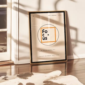 Può includere: Un poster incorniciato con la parola "FOCUS" in un design a cerchio e quadrato. Il poster ha uno sfondo beige con bordi neri e dorati. Il testo "FOCUS ON WHAT MATTERS" è in basso.
