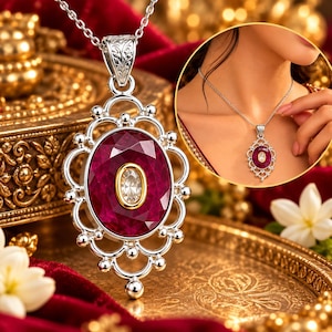 Pode incluir: Um colar com pendente de prata apresentando uma grande pedra preciosa oval de cor vermelho-profundo facetada, com uma pedra oval mais pequena e clara engastada num bisel dourado ao centro. A moldura de prata tem um design de filigrana.