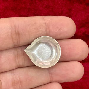 Peut inclure: Un petit plat argenté en forme de goutte d'eau. Le plat a une cuvette peu profonde et une extrémité pointue. La surface du plat est lisse et réfléchissante. Le plat est probablement en métal et est tenu dans une main.