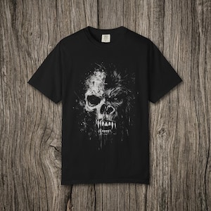 May include: A black short-sleeved t-shirt featuring a white graphic print on the chest. The design displays a split face, with one side showing a human skull and the other side showing a gorilla face, both rendered in a distressed, ink-splatter style.