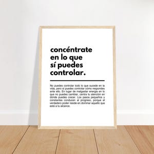 May include: A framed print with the text "concéntrate en lo que sí puedes controlar." in black against a white background. The print is in a light wood frame and is displayed on a wooden surface.