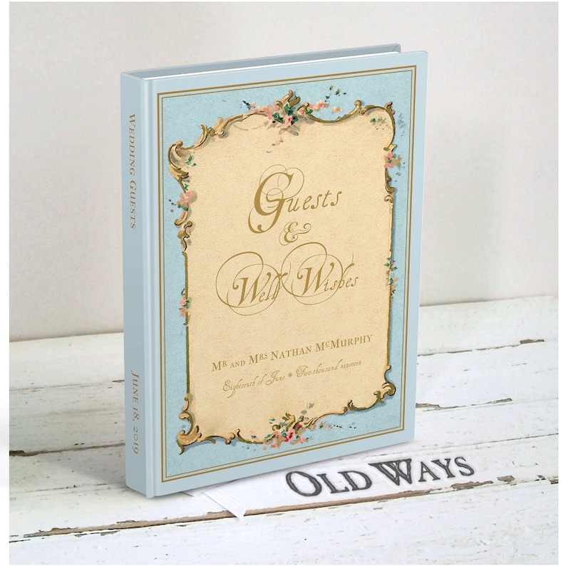 May include: A light blue wedding guest book with a gold and floral design. The cover reads "Guests & Well Wishes" and "Mr. and Mrs. Nathan McMurchy" with the date "June 18, 2019". The book is titled "Old Ways" on the bottom.