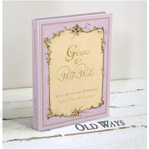 May include: A lavender-colored book with a gold-trimmed cover and floral accents. The title is "Guests & Well Wishes" with the text "Mr. and Mrs. Nathan McMurchy" and "June 18, 2019" on the cover. The book is titled "Old Ways" on the bottom.