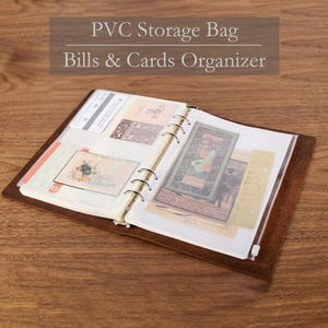 Può includere: Raccoglitore in pelle marrone aperto con tasche portaoggetti in PVC trasparente piene di carte ed effimeri. Il raccoglitore ha anelli metallici e una chiusura a cerniera. Il testo in alto recita "PVC Storage Bag Bills & Cards Organizer."