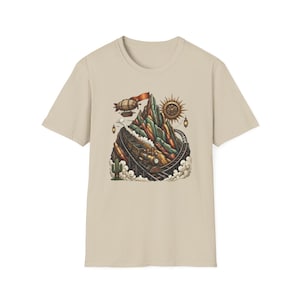 May include: A beige t-shirt featuring a colorful illustration of a mountain with a train, blimp, and sun. The design has a steampunk aesthetic with a vintage feel. The shirt is made of a soft material.