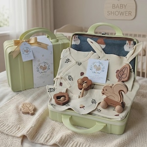 May include: A light green suitcase gift set containing a cream-colored baby outfit with leaf patterns, a dark blue blanket with squirrel prints, a wooden squirrel toy on wheels, a wooden acorn rattle, a leaf-shaped wooden teether, and a card.