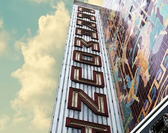 May include: A vintage-style sign for the Paramount Theater, with red neon letters against a silver background. The sign is mounted on the side of a building with a colorful mosaic mural.