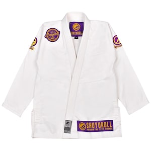 Puede incluir: Uniforme de artes marciales blanco con detalles morados y dorados. El uniforme presenta el texto "SHOYOROLL" en el pecho, las mangas y el dobladillo. Diseñado para entrenamiento y competición de artes marciales.