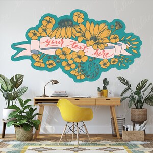 May include: A teal blue and yellow floral design with a pink banner that says "your text here". The design is on a white wall above a wooden desk with a yellow chair.