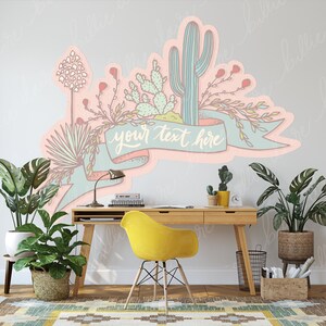 May include: A pastel pink and blue cactus and succulent wall decal with a banner that says "your text here". The decal is on a white wall above a wooden desk with a yellow chair.