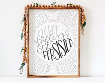 Puede incluir: Una impresión enmarcada con un fondo blanco y un círculo gris y negro con el texto "nevertheless she persisted" en un estilo de escritura a mano.