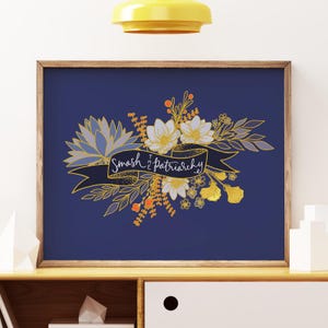 May include: A framed art print with a navy blue background. The artwork features a floral arrangement in gold, white, and orange hues, with a banner that reads "Smash the Patriarchy" in white script. The frame is a warm brown color.