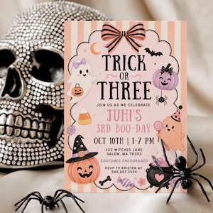 May include: A rectangular party invitation card with a light pink and white striped background, featuring a large bow at the top and the text Trick or Three. The design includes illustrations of ghosts, pumpkins, a cauldron, and candy, with event details for Juhi's 3rd Boo-Day on Oct 10th.