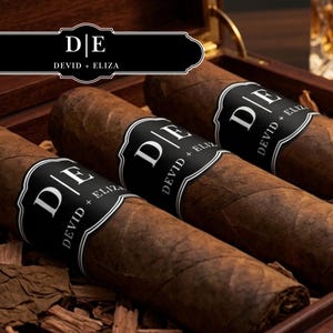 May include: Three brown cigars with black labels, each bearing the initials "D E" and the names "DEVID + ELIZA". The cigars are presented in a wooden box, with tobacco leaves visible. The image has a warm, inviting tone.