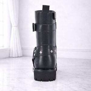 May include: Black leather boot with multiple straps, buckles, and decorative studs. The boot has a chunky sole and a mid-calf height. The text "The Ultimate Leather" is at the bottom of the image.