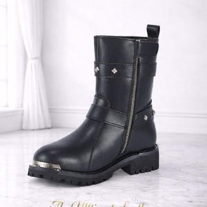 May include: Black leather ankle boot with a side zipper, studded accents, and buckle straps. The boot has a silver-toned toe cap and a lug sole. The text "The Ultimate Leather" is at the bottom.