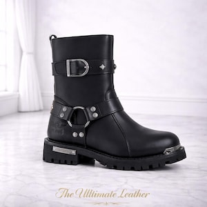 May include: Black leather motorcycle boot with silver-tone hardware, including buckles, studs, and a metal toe cap. The boot features a chunky sole and a harness detail. The text "The Ultimate Leather" is at the bottom.