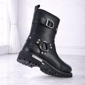 May include: Black leather boot with silver-tone buckles and studs. The boot features a chunky sole and a harness-style strap. The text "The Ultimate Leather" is at the bottom of the image.