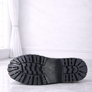 May include: Black leather boot sole with a deep tread pattern. The sole features a circular emblem and the text "The Ultimate Leather" in gold.