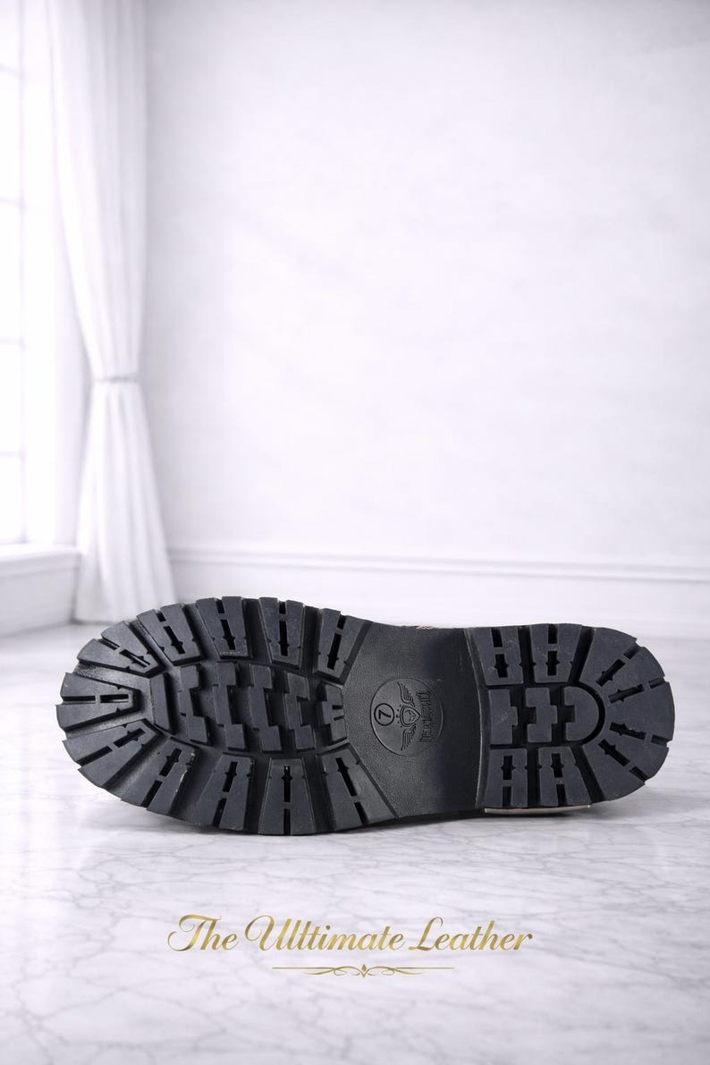 May include: Black leather boot sole with a deep tread pattern. The sole features a circular emblem and the text "The Ultimate Leather" in gold.