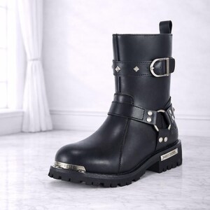 May include: Black leather boot with silver-tone hardware, including buckles, studs, and a decorative plate. The boot features a short shaft and a lug sole. The text "The Ultimate Leather" is at the bottom.
