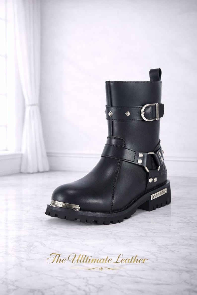 May include: Black leather boot with silver-tone hardware, including buckles, studs, and a decorative plate. The boot features a short shaft and a lug sole. The text "The Ultimate Leather" is at the bottom.