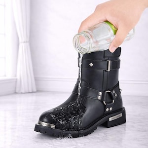 May include: Black leather boot with silver hardware, including buckles, rings, and studs. Water is poured onto the boot, demonstrating its waterproof feature. The text "The Ultimate Leather" is at the bottom.